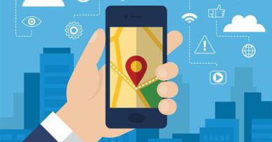 Imagem de uma mão segurando um celular. Ao fundo prédios e algumas nuvens, Na tela do celular está desenhado um ícone que indica a localização. 