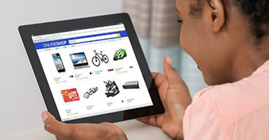 Foto. Mulher negra, vestindo blusa rosa. Ela segura um tablet na mão. Na tela do tablet está aberta uma página de e-commerce. 