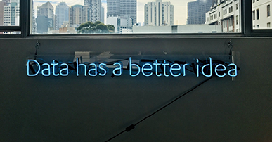 Imagem: Janela com vista para prédios e led escrito"data has a better idea". ferramentas de e-mail marketing.