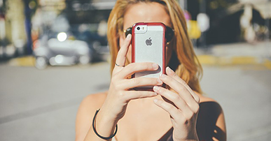 Imagem: mulher loira segurando celular na frente do rosto.