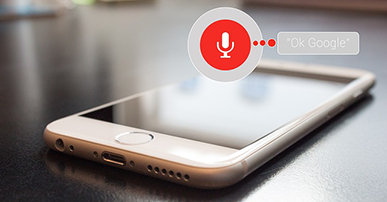 Imagem: Celular em cima da mesa com um balão de conversa e as palavras "ok Google".dispositivos de voz.
