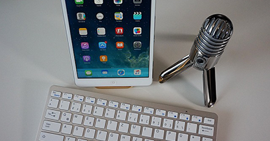 Imagem: tablet com teclado e microfone em cima da mesa. Podcast.