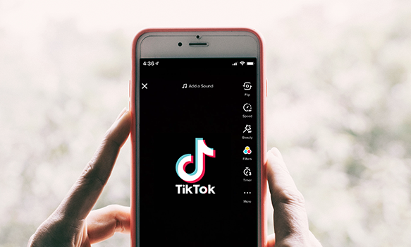 Imagem: pessoa segurando um celular com logo do app TikTok na tela.